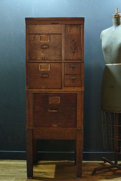 an old chest of drawers next to a mannequin on a wooden floor in front of a blue wall