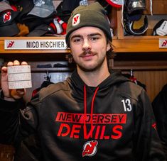 a man in a black hoodie is holding up a white card with the name of his team