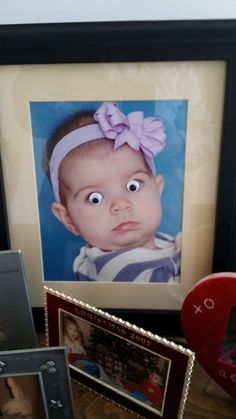 there is a framed photo and two pictures on the table next to each other with an odd looking baby's face