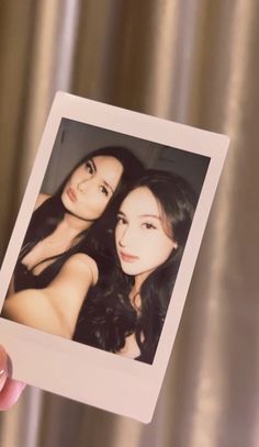 two women are posing for the camera with one holding up an old polaroid photo