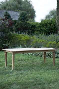 a wooden table sitting on top of a lush green grass covered field next to trees