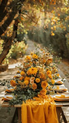 a long table is set with yellow flowers and place settings for an outdoor dinner party