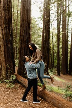 a man holding a woman on his back in the woods while they are standing on a log