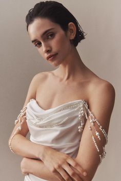 a woman in a white dress with pearls on her arm and arms wrapped around her shoulder