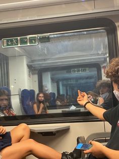 two people sitting on a train with their hands up to the window and one person wearing a face mask