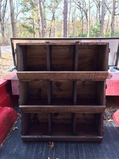 the back end of a red truck with wooden shelves on it's sides and trees in the background