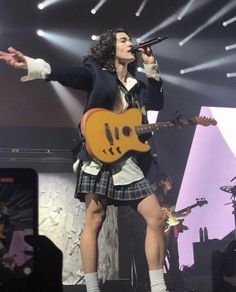 a woman singing into a microphone and holding a guitar in her hand while standing on stage