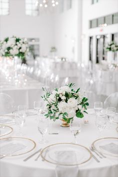 a table with white flowers and gold rimmed glasses on it is set for a formal dinner