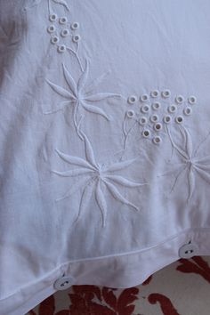 an embroidered white pillow with buttons on the bottom and sides, sitting on a floral patterned cushion