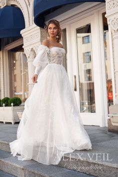 a woman in a white wedding dress standing on some steps wearing an off the shoulder gown