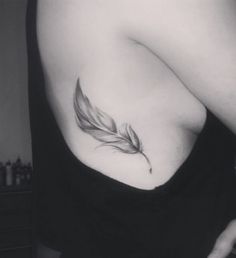 a black and white photo of a woman's shoulder with a feather tattoo on it