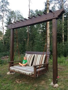 a young boy sitting on a wooden swing in the middle of some grass and trees