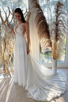 a woman standing in front of a window wearing a white wedding dress with long train