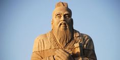 a statue of an old man with a long beard and wearing a hat, standing in front of a blue sky