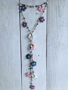 a necklace with flowers hanging from it on a white wooden surface, next to a pair of scissors