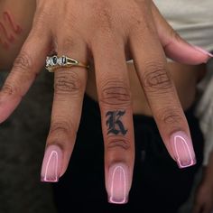 a woman's hand with pink nail polish and tattoos on her left thumb, showing the ring finger