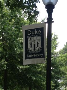 a lamp post with a duke banner hanging from it's side in front of trees