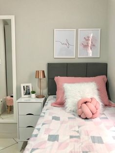 a bed with pink and grey pillows on it in a bedroom next to two framed pictures