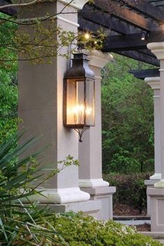 a lantern hanging from the side of a pergolated covered patio with trees in the background