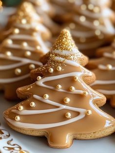 cookies decorated like christmas trees on a plate with gold trimmings and white frosting