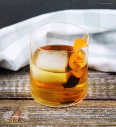 a glass filled with ice and orange peels on top of a wooden table next to a napkin