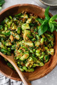 a wooden bowl filled with cucumber salad and topped with fresh mint leaves on the side