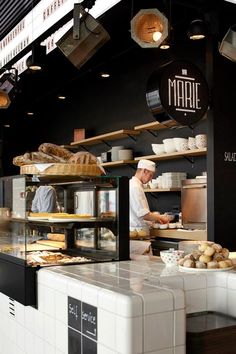 a man preparing food inside of a kitchen next to shelves filled with bread and pastries