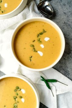 two bowls filled with soup sitting on top of a table next to silver spoons