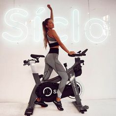 a woman standing on an exercise bike in front of a neon sign that reads silo