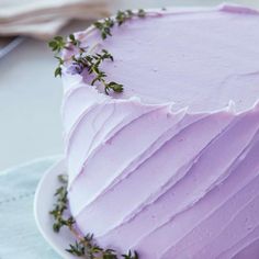 a cake with lavender frosting and greenery on the top is sitting on a plate