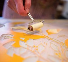 a person using a paint roller on a piece of paper with yellow and white designs