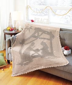 a white crocheted afghan sitting on top of a couch next to a window