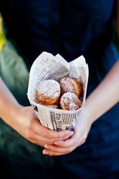 a woman holding a paper basket filled with donuts covered in powdered sugar and sprinkled with icing