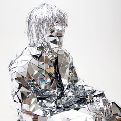 a woman made out of mirrors sitting on top of a white floor next to a wall