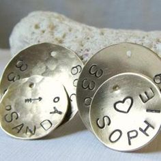 three personalized silver discs with names and hearts are on a white surface next to a rock