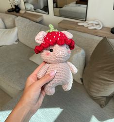 a hand holding a small crocheted teddy bear with a red hat on it's head