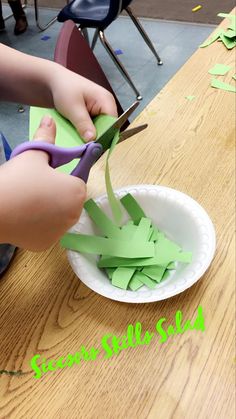 a child cutting paper with scissors on top of a wooden table in front of other children