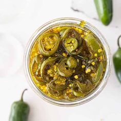 an overhead view of pickles and peppers in a glass jar on a white surface