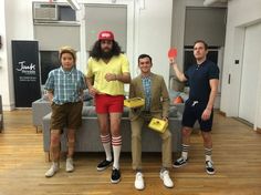 three men are standing in front of a couch holding frisbees and posing for the camera