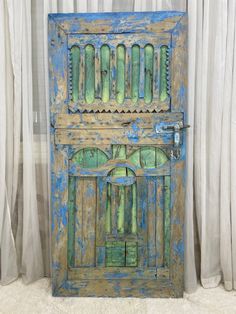 an old blue and green wooden door sitting on top of a white curtained wall