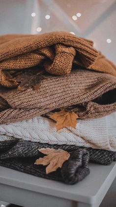 a pile of sweaters and scarves sitting on top of a white table with lights in the background