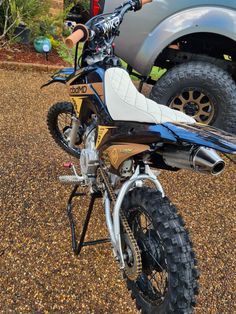 a dirt bike parked on top of a gravel road next to a gray pickup truck