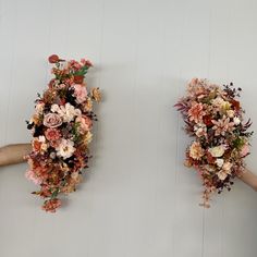 two hands holding flowers against a white wall