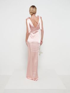 the back of a woman in a pink dress standing against a white wall with her hands on her hips