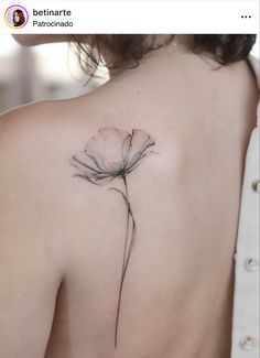 the back of a woman's shoulder with a single flower tattoo on her left shoulder