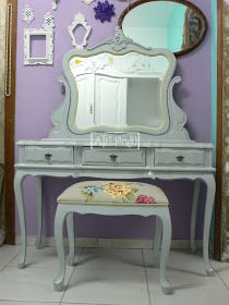 a vanity with a mirror and stool in front of it on the floor next to a purple wall