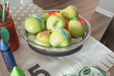 there is a bowl of apples on the table with markers and pencils next to it