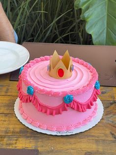 a pink and blue cake with a crown on top sitting on a table next to a plate