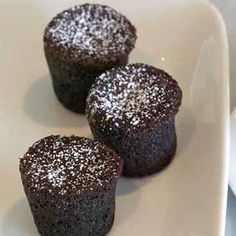 three chocolate cupcakes on a white plate with powdered sugar sprinkled on top