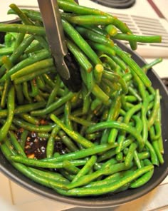 green beans being cooked in a skillet with tongs on the stove burner